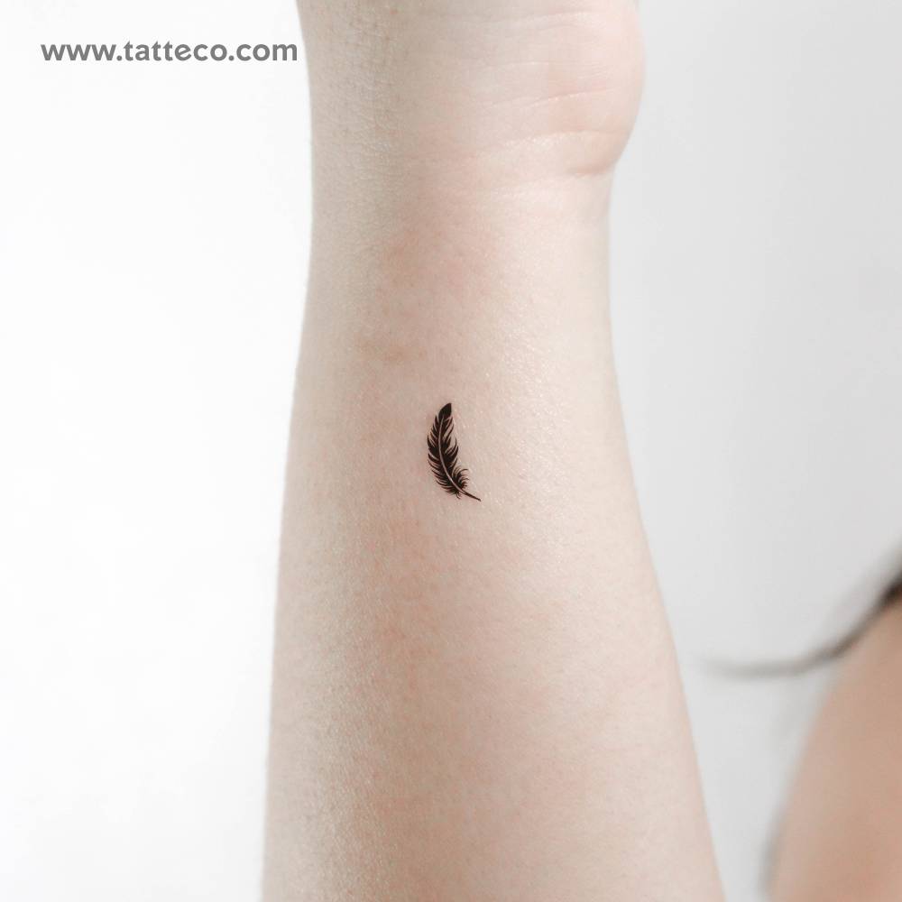 Tiny black feather temporary tattoo located on the wrist.