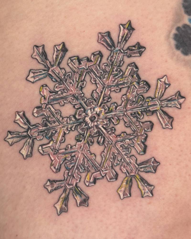 Snowflake tattoo in illustrative style located on the thigh.