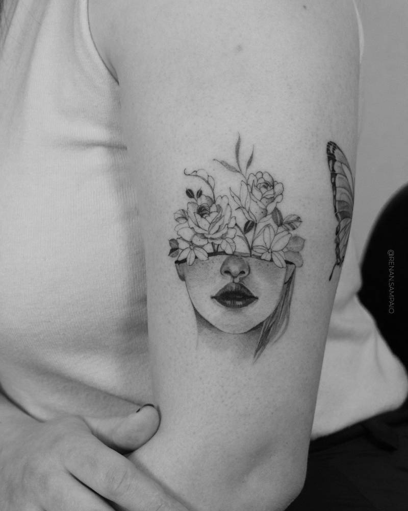 Flower head woman tattooed on the upper arm.