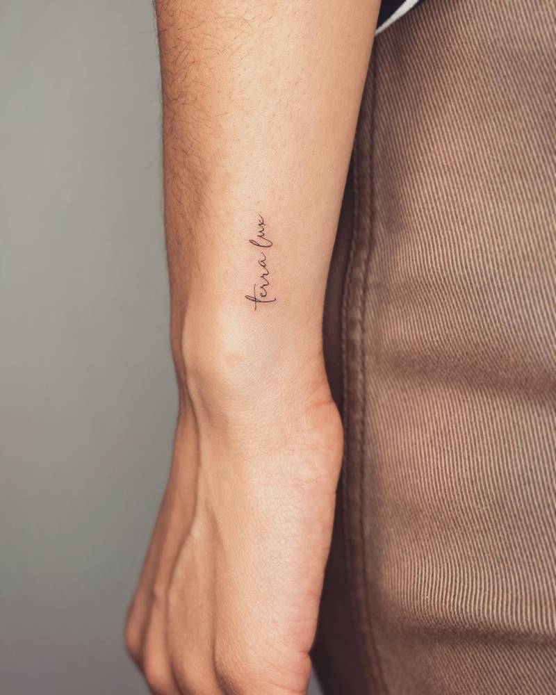"Terra lux" lettering tattoo handwritten on the wrist.