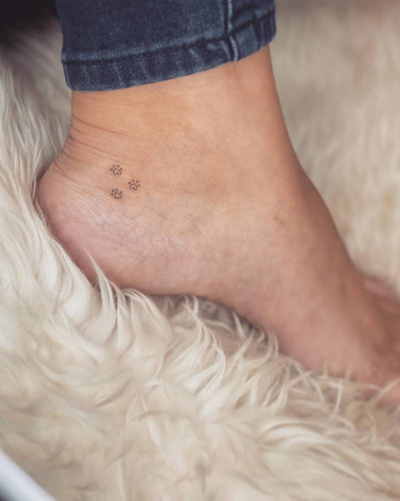 Tiny minimalistic dog paws tattooed on the ankle.