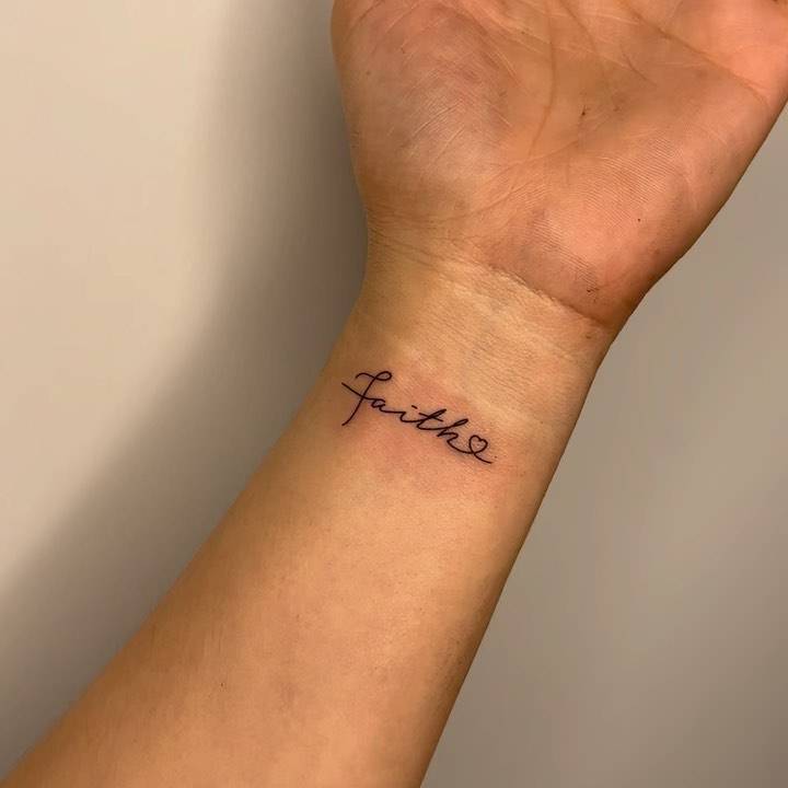 Tattoo of the word "faith" handwritten on the wrist.