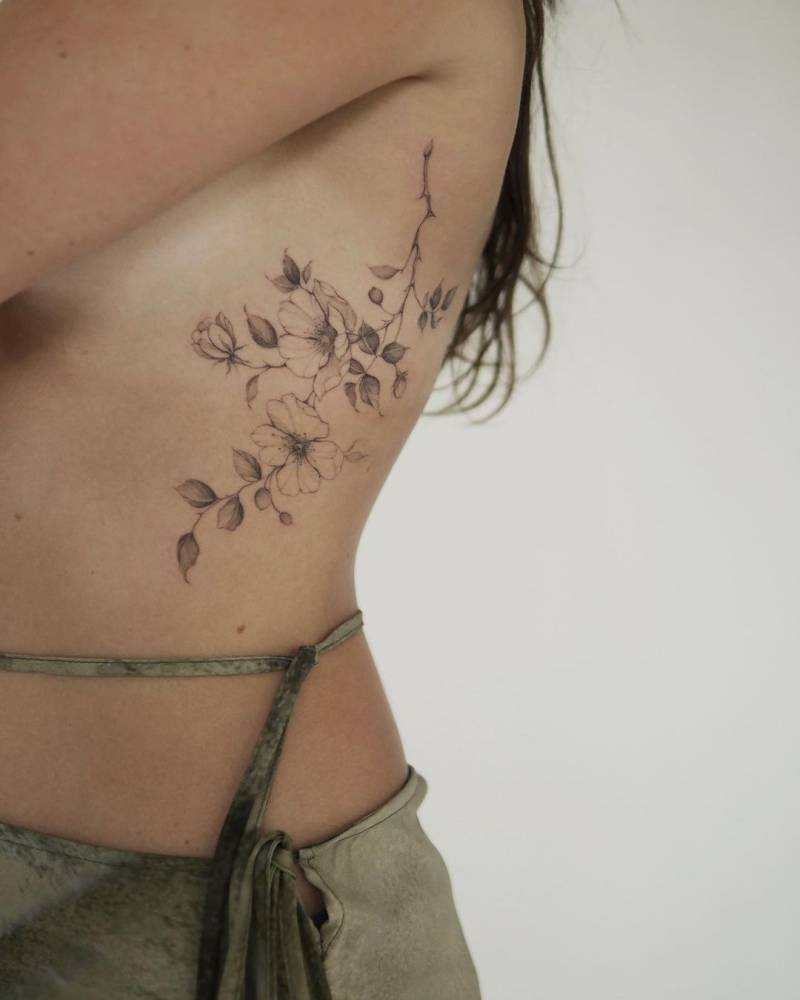 Dog rose tattoo located on the rib, illustrative style.
