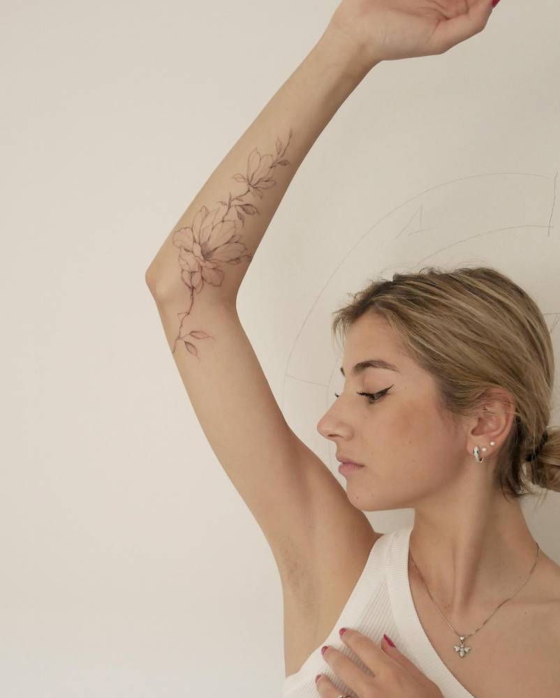 Freehand magnolia tattoo located on the arm, illustrative style.