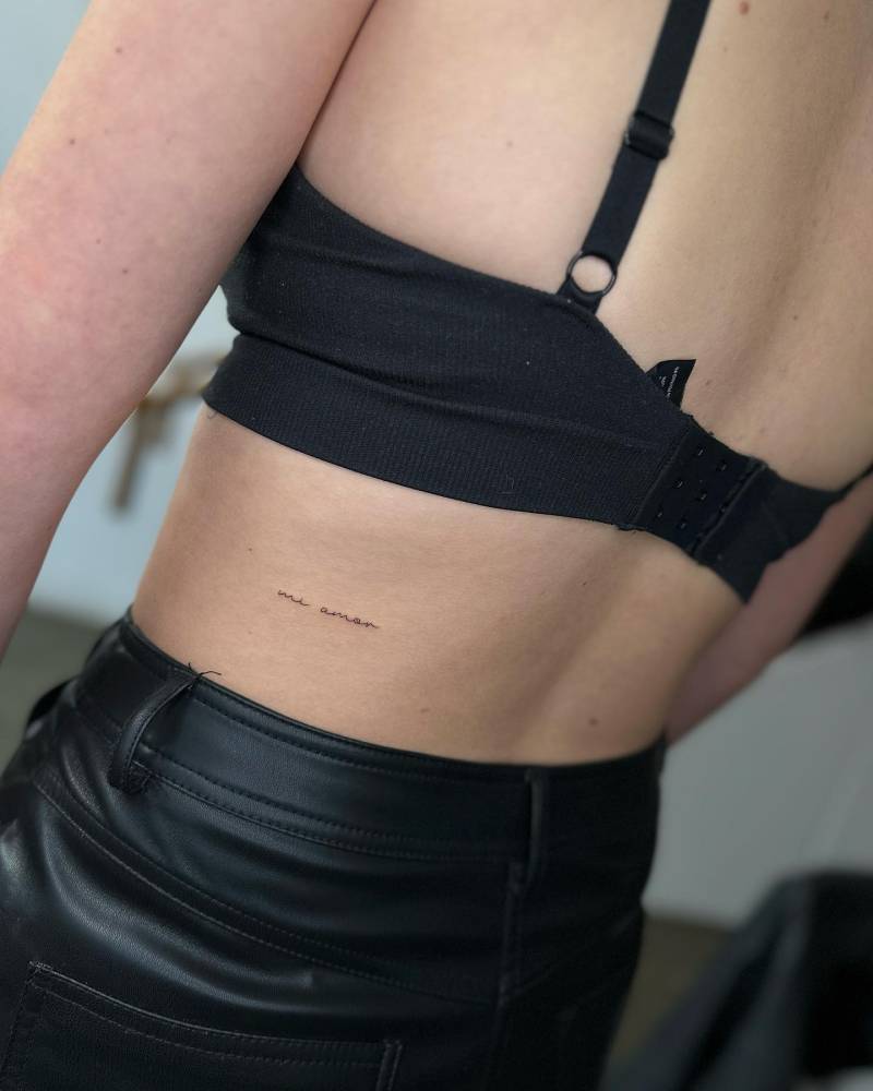 Tattoo that says "mi amor" located on the lower back.