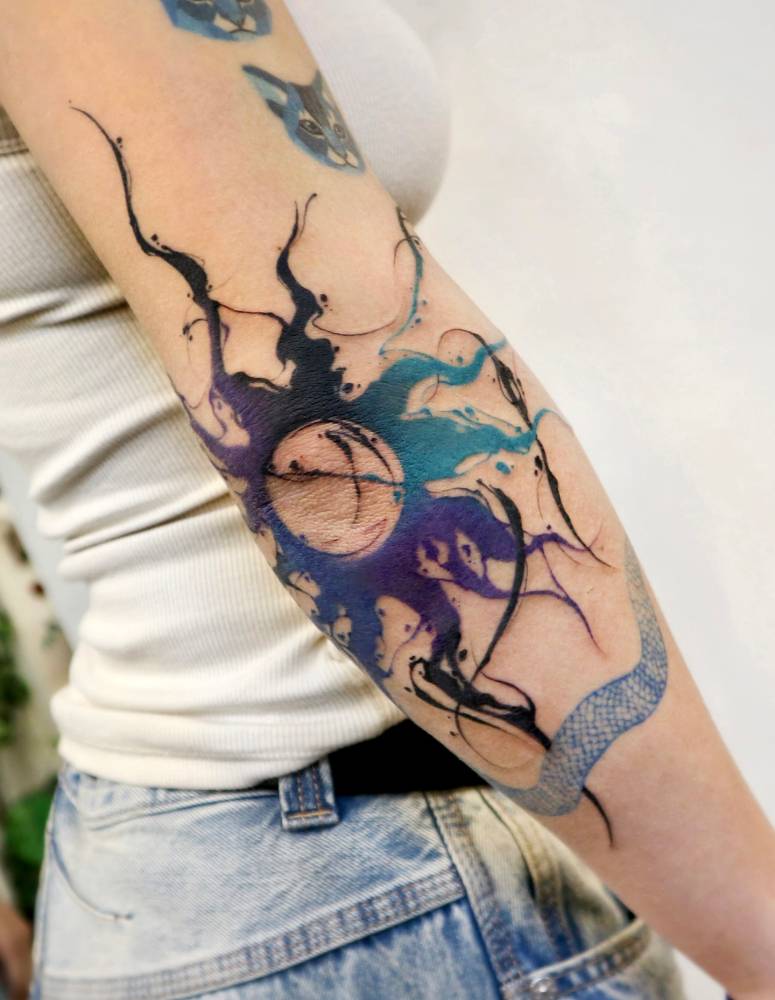 Watercolor style abstract sun tattoo located on the elbow.