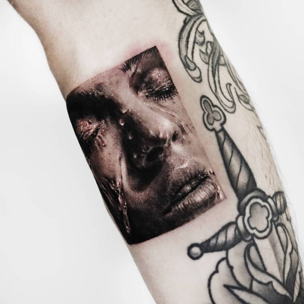 Micro-realistic style face tattoo located on the inner forearm.