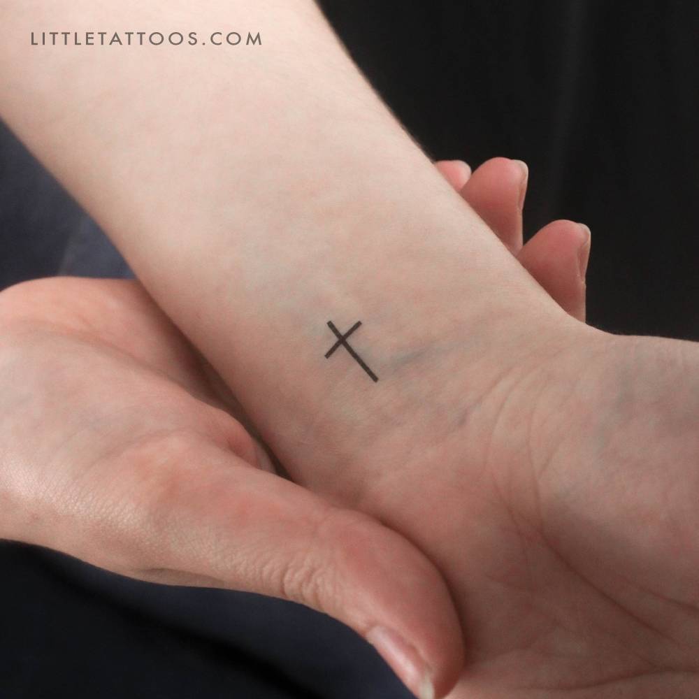 Tiny minimalist cross temporary tattoo located on the wrist.