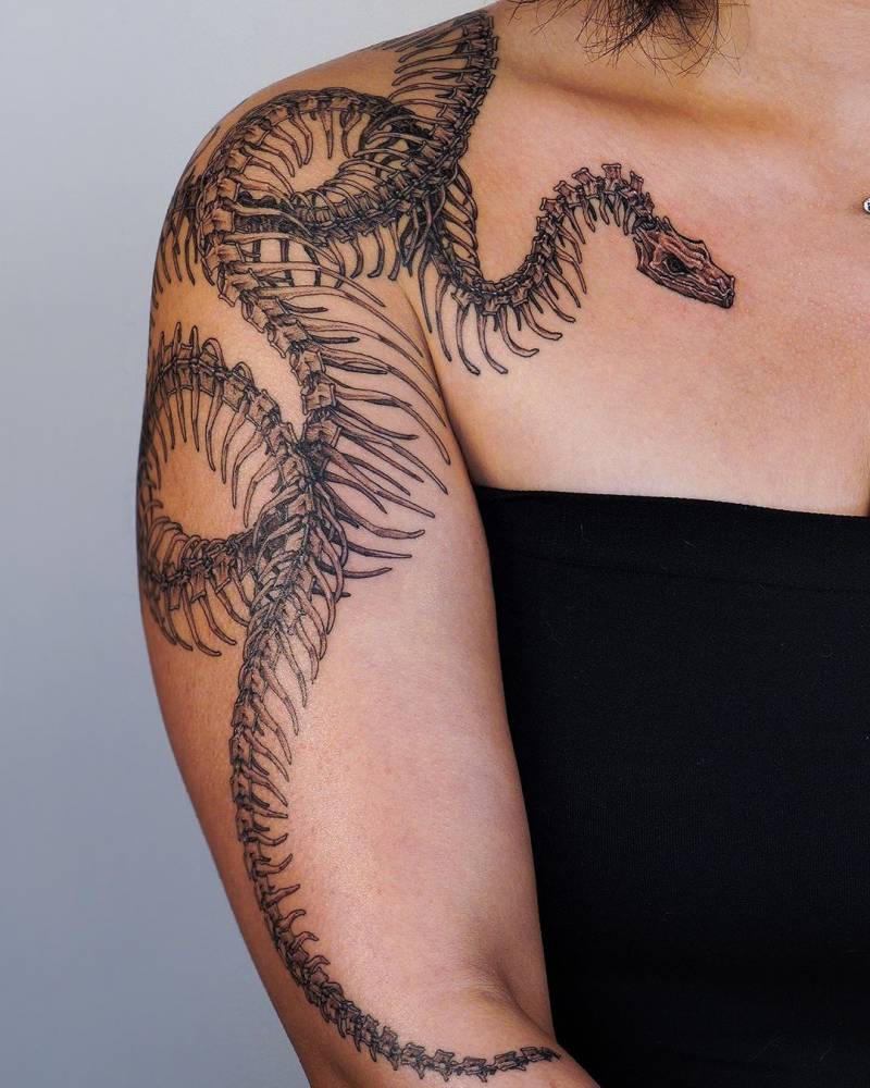 Skeleton snake tattoos located on the shoulder and upper arm.