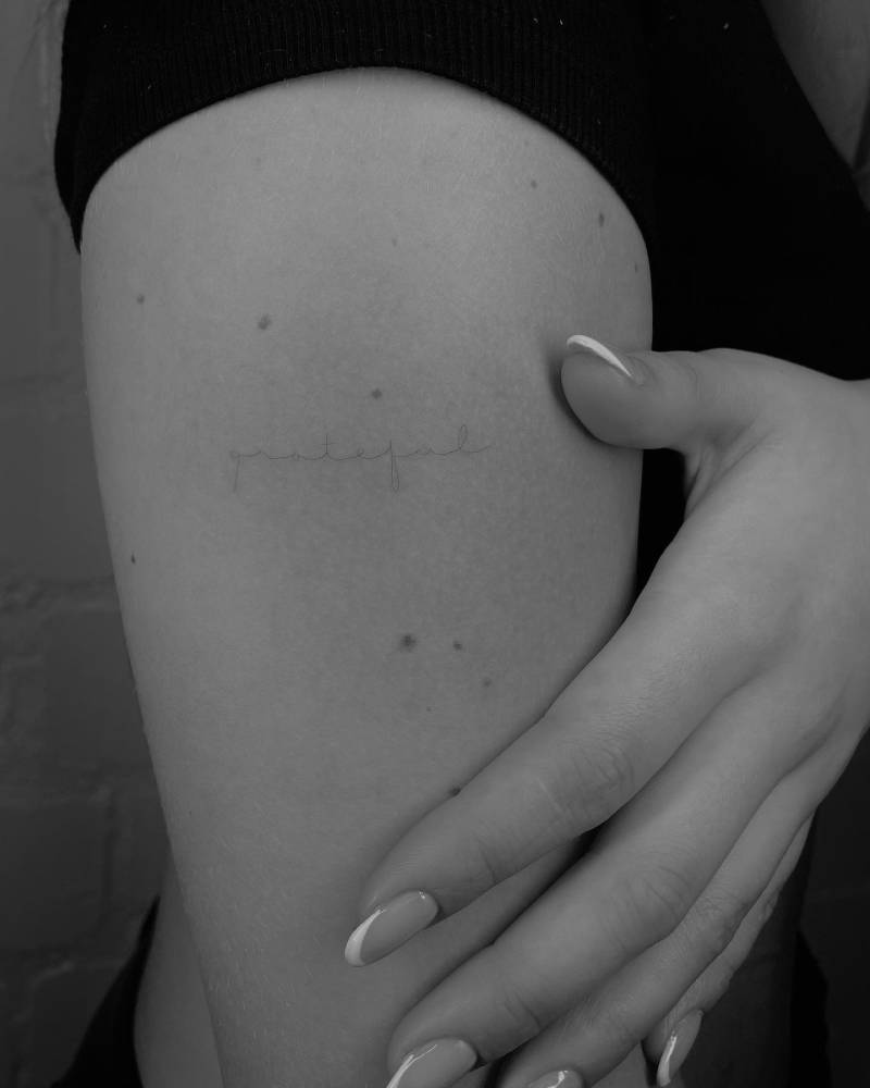 Tattoo of the word "grateful" handwritten on the upper arm.
