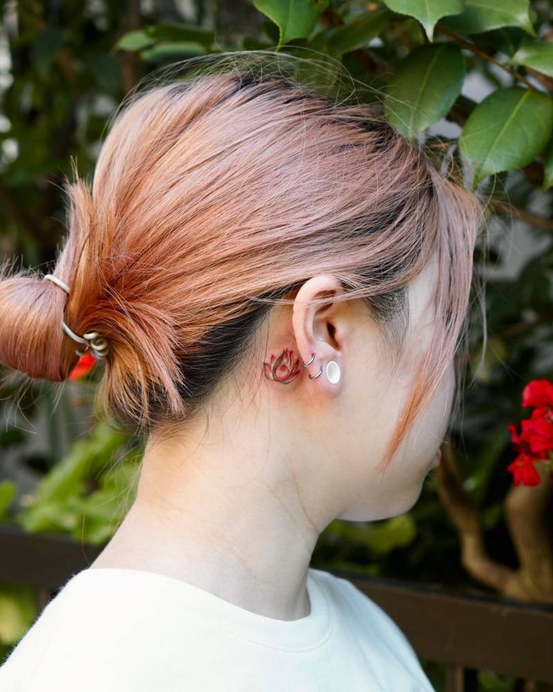 Watercolor style lotus flower tattoo placed behind the ear.