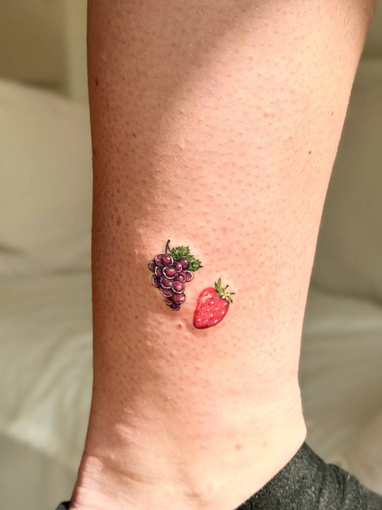 Grapes and strawberry tattoo in illustrative style located on the ankle.