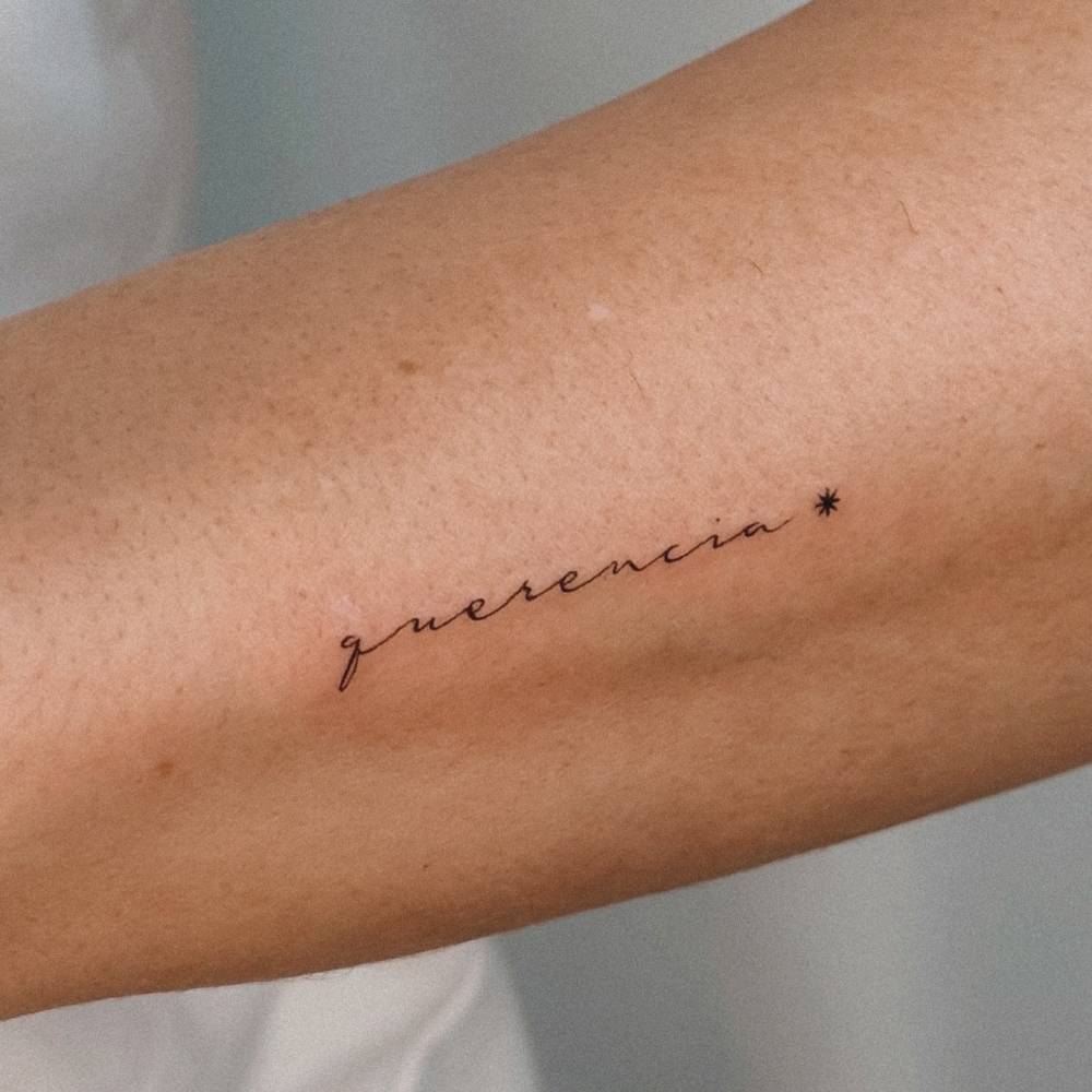 "Querencia" lettering tattoo in script font located on the forearm.