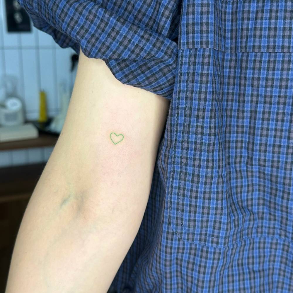 Green heart tattoo in minimalistic style hand poked on the inner arm.