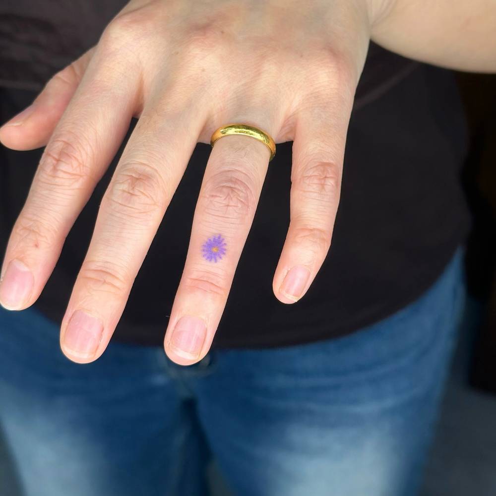 Minimalistic purple flower tattoo hand poked on the finger.