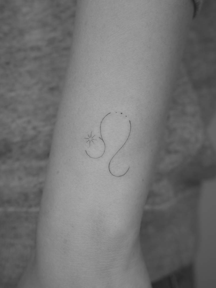 Fine line style Leo zodiac symbol tattoo placed on the wrist.