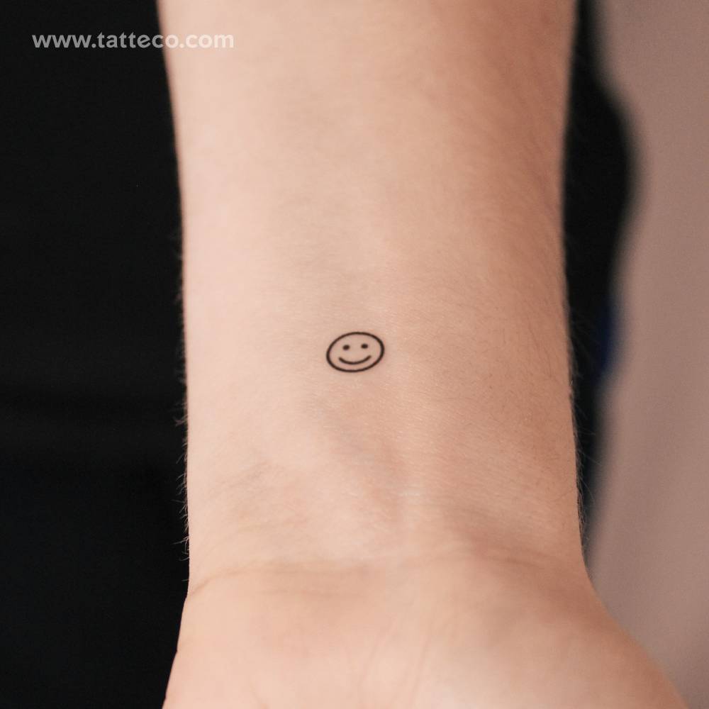 Tiny minimalist smiley semi-permanent tattoo located on the wrist.
