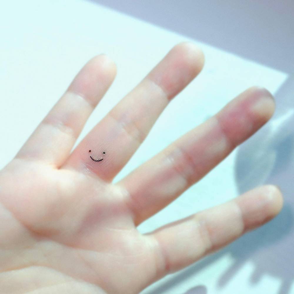 Minimalistic style smiley face tattoo done on the finger.