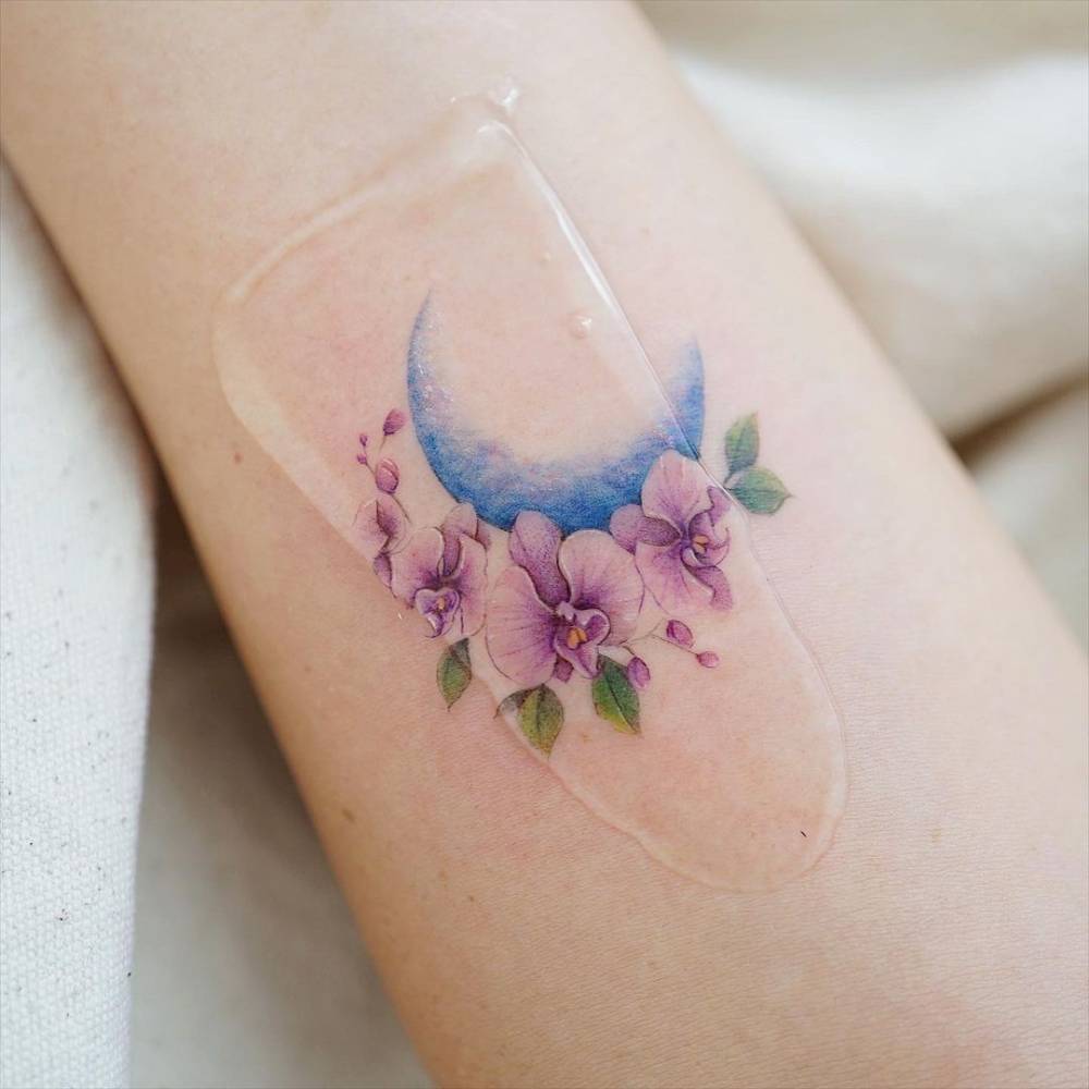 Watercolor flower moon tattoo on the inner forearm.