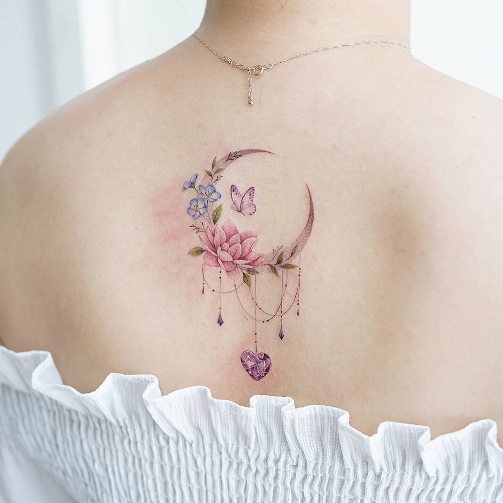 Watercolor flower moon tattoo on the upper back.