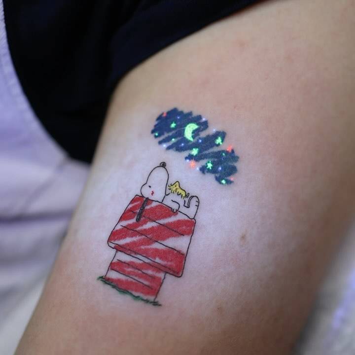 Snoopy and Woodstock tattoo in cartoon style located on the upper arm.