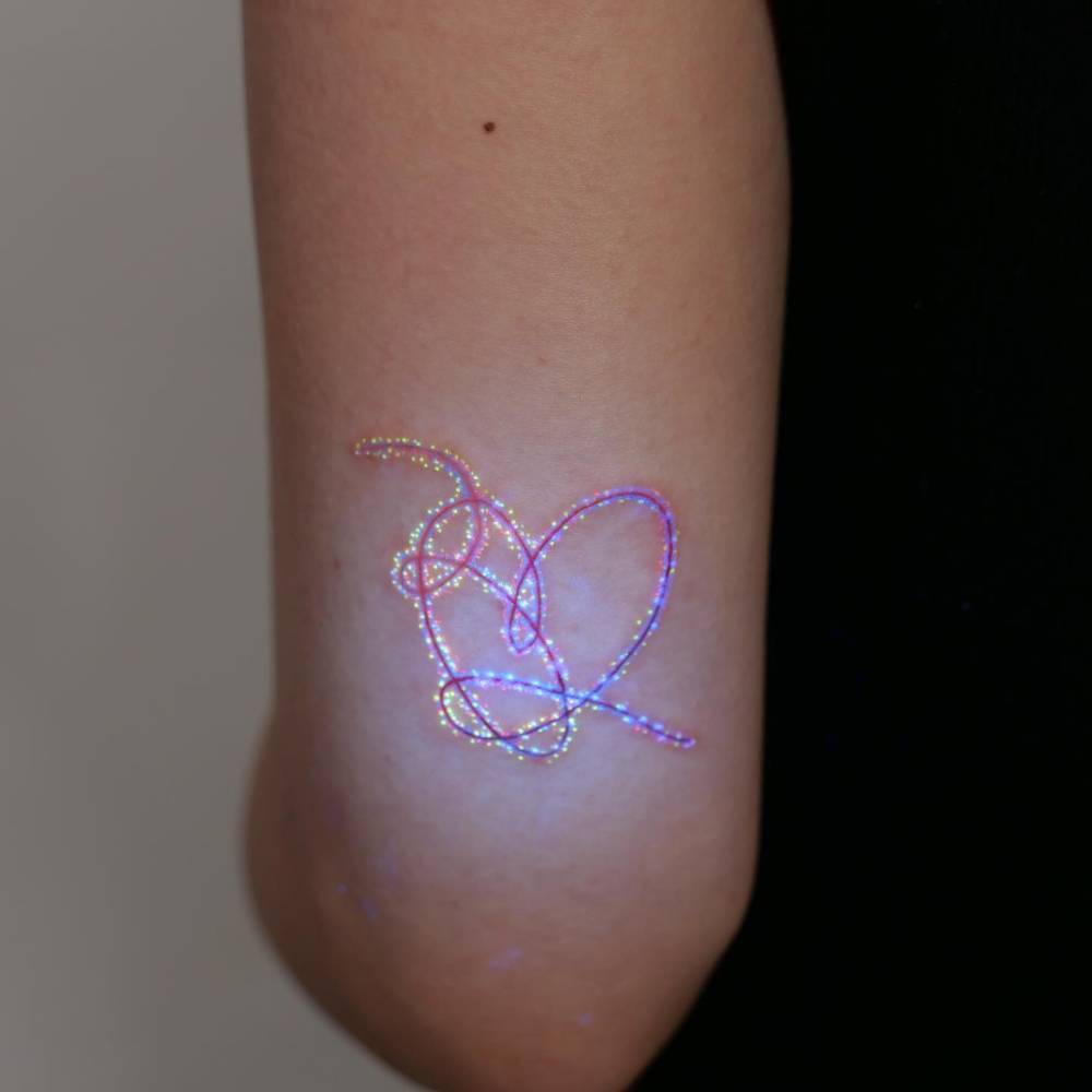 BTS heart tattoo in UV ink located on the tricep.