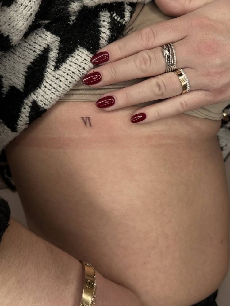 Roman numeral tattoo located on the rib, minimalistic style.