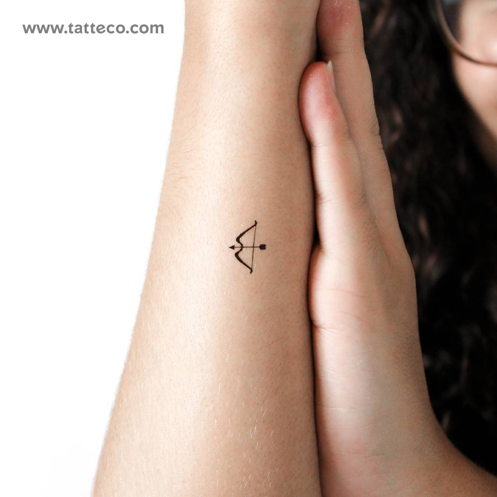 Tiny minimalistic bow and arrow temporary tattoo located on the wrist.