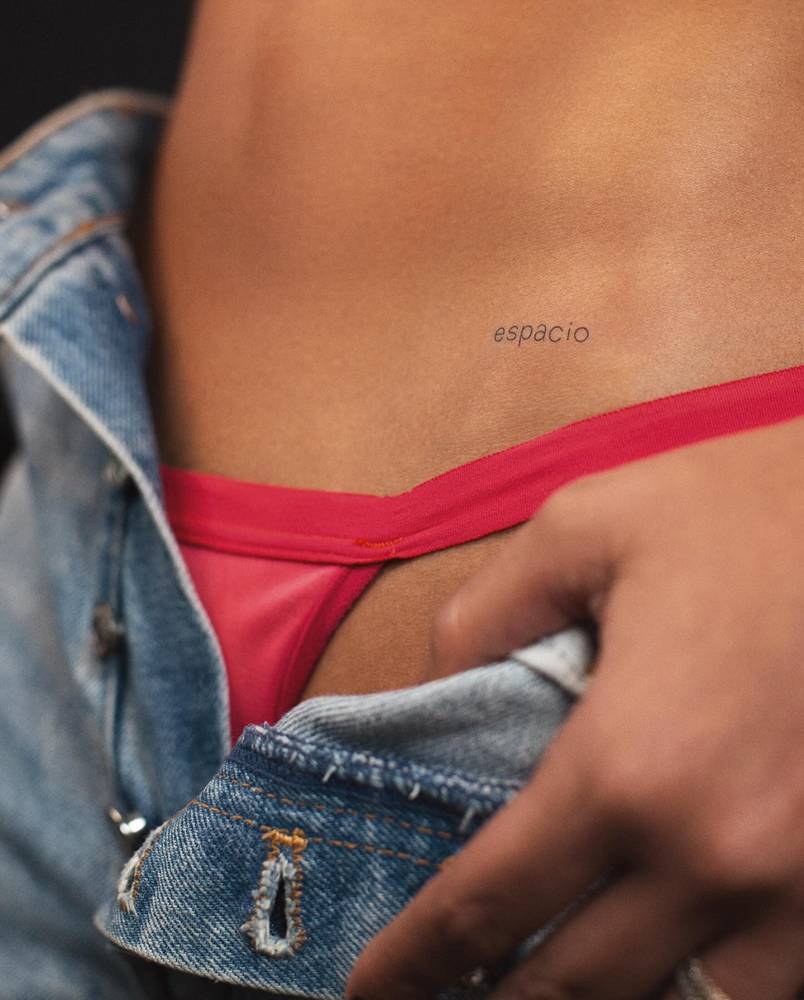Lettering tattoo of the word "espacio" located on the pelvis.