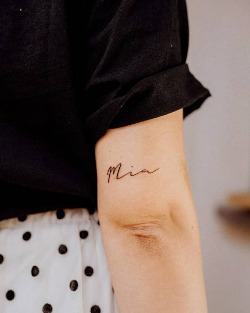 "Mia" lettering tattoo on the tricep.