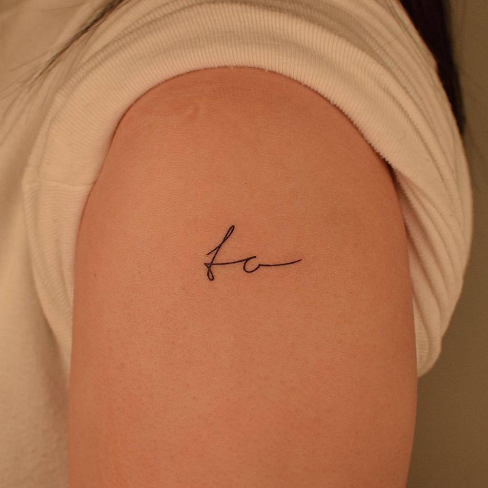 "To" lettering tattoo on the upper arm.