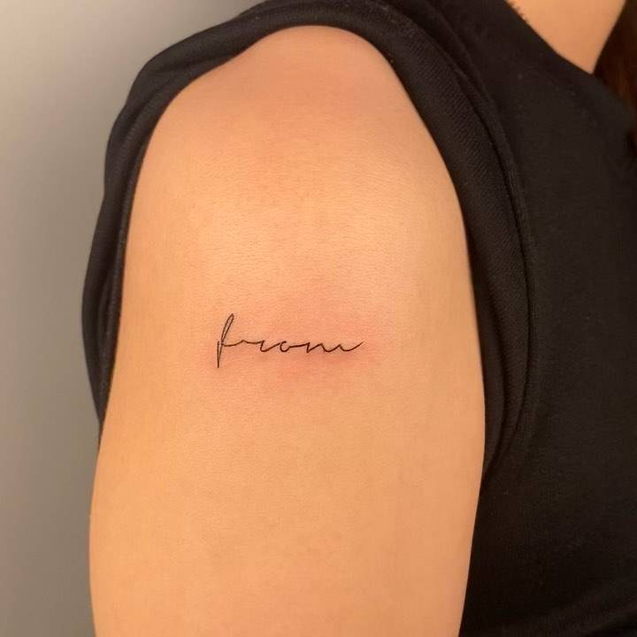 "From" lettering tattoo on the upper arm.