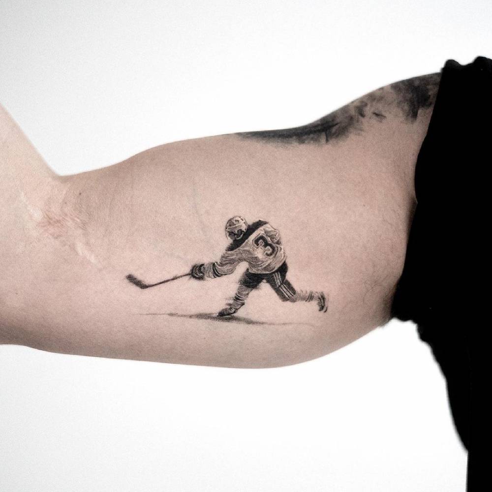 Micro-realistic hockey player tattoo on the inner arm.