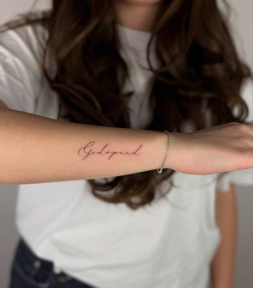 "Godspeed" lettering tattoo in script font placed on the wrist.