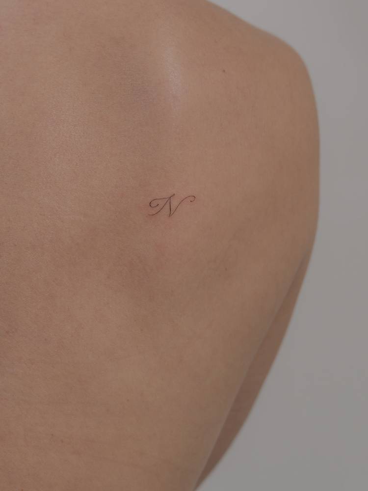 Little letter "N" tattoo located on the shoulder.