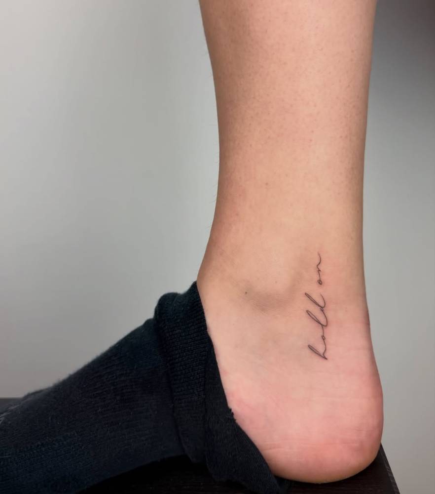 "Hold on" lettering tattoo in script fone located on the ankle.