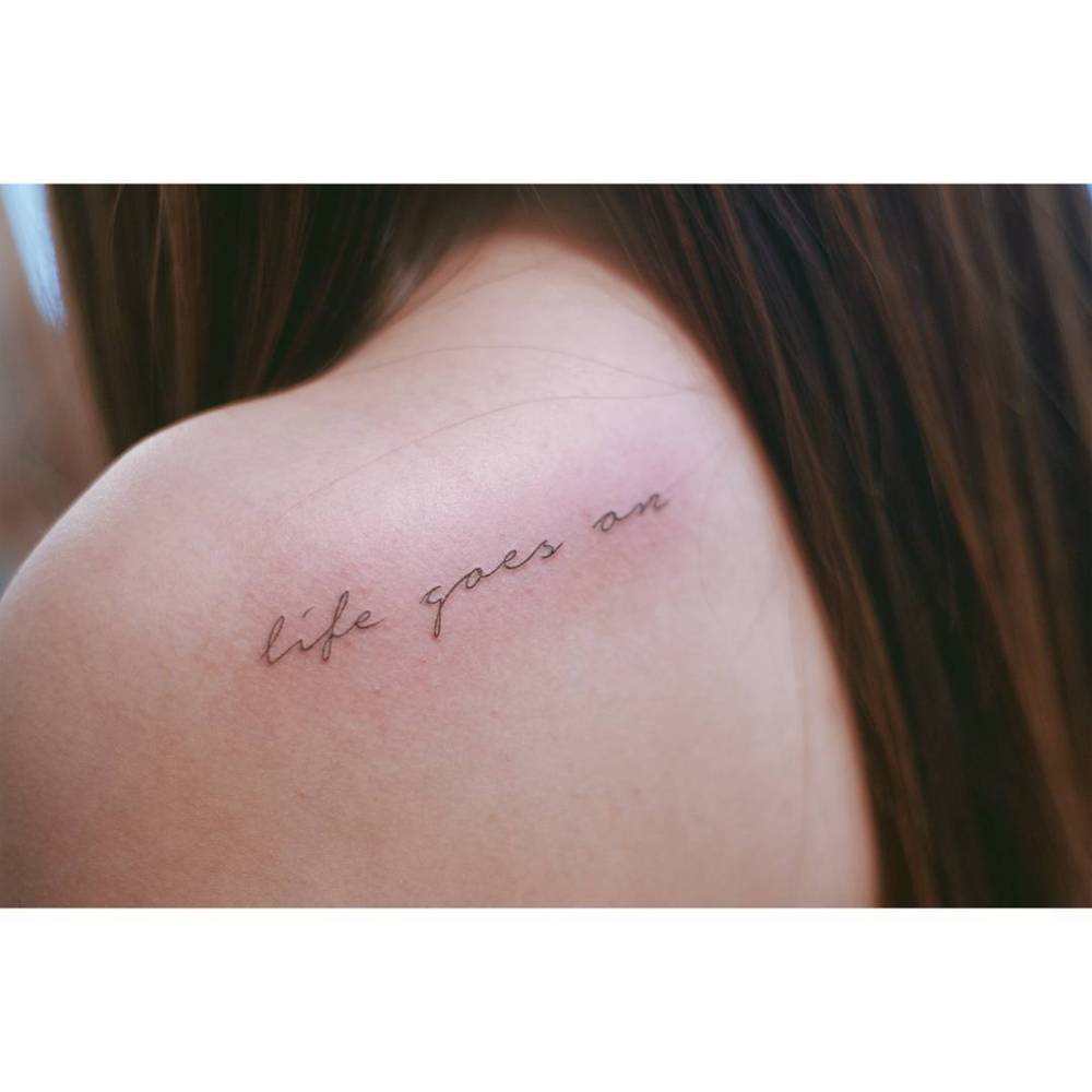 "Life goes on" lettering tattoo placed on the shoulder blade.