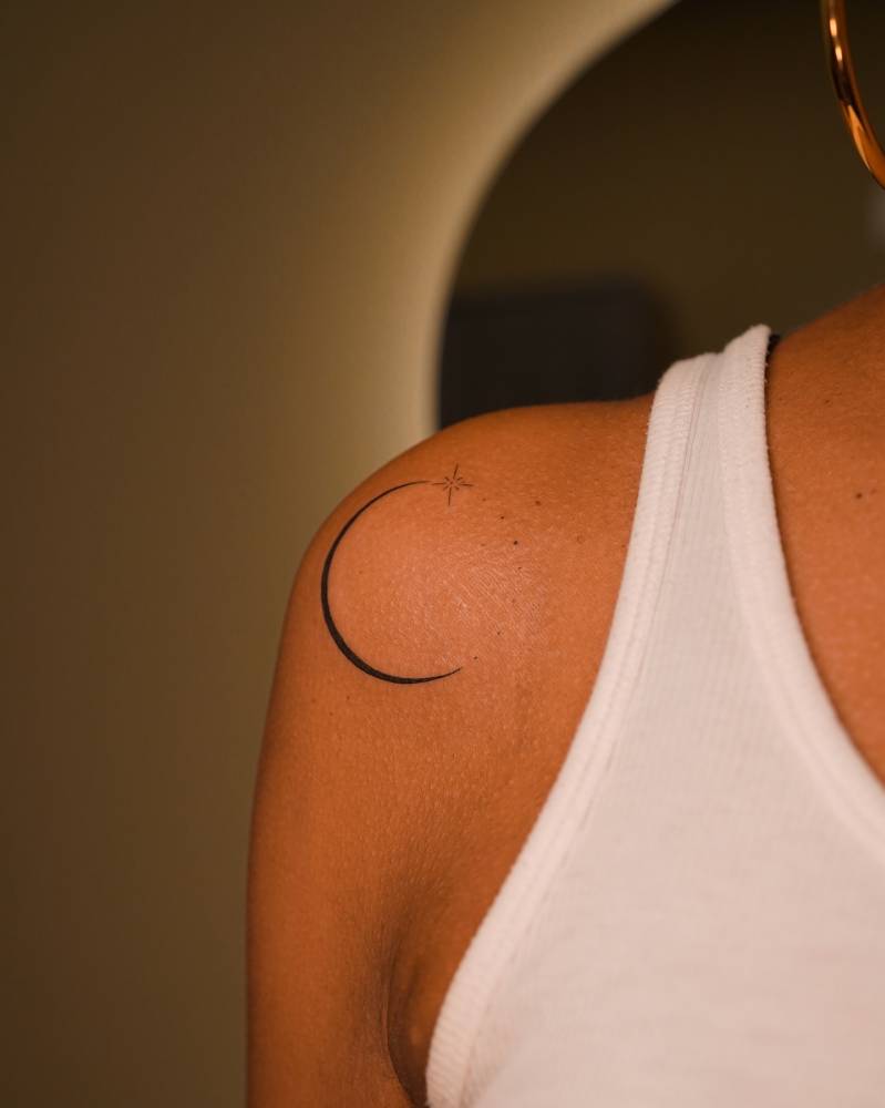 Crescent moon tattoo located on the shoulder, minimalistic style.