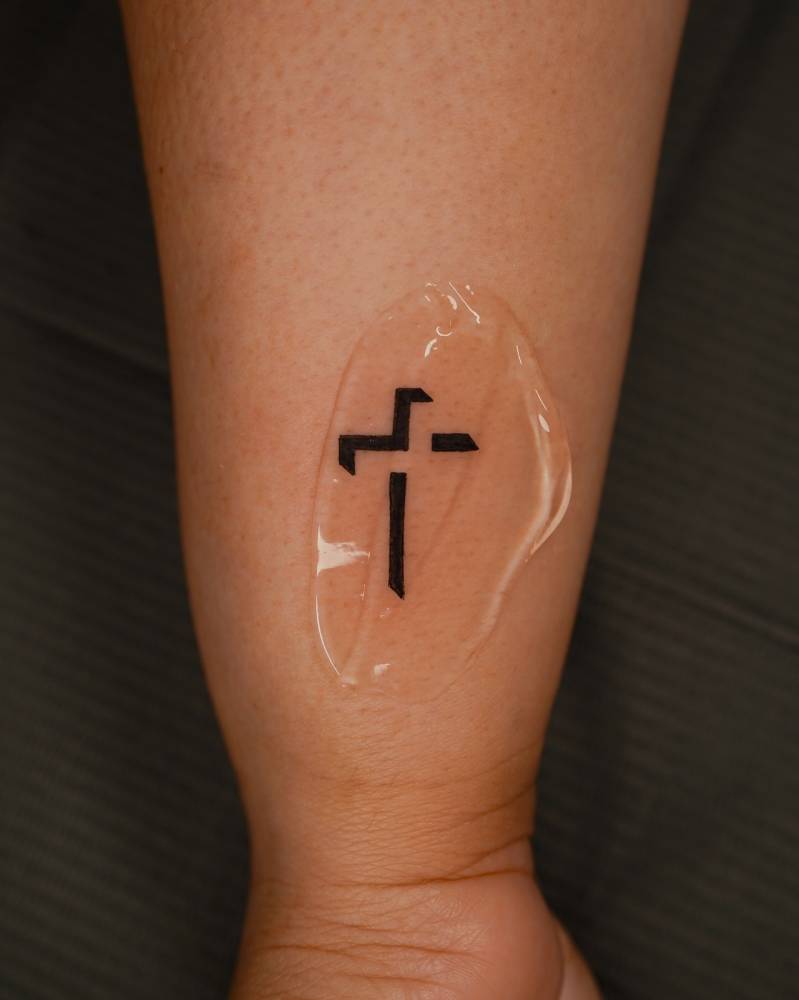 Cross tattoo located on the wrist, done in minimalistic style.