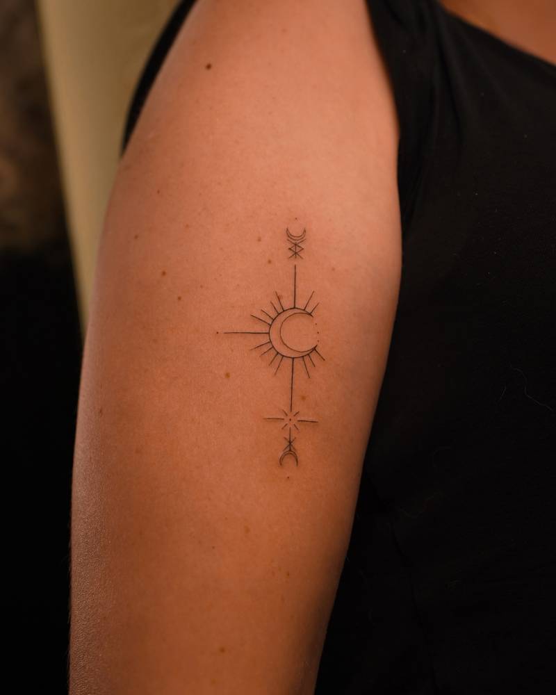 Ornamental crescent moon tattoo in fine line style located on the upper arm.