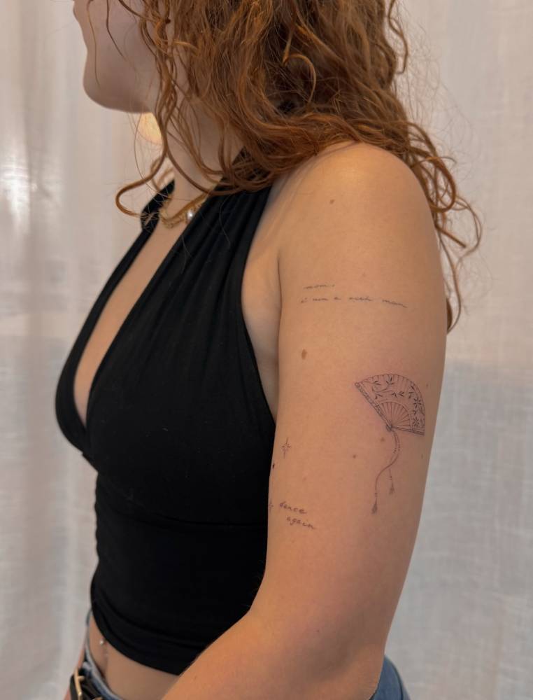 Hand fan tattoo in fine line style located on the upper arm.