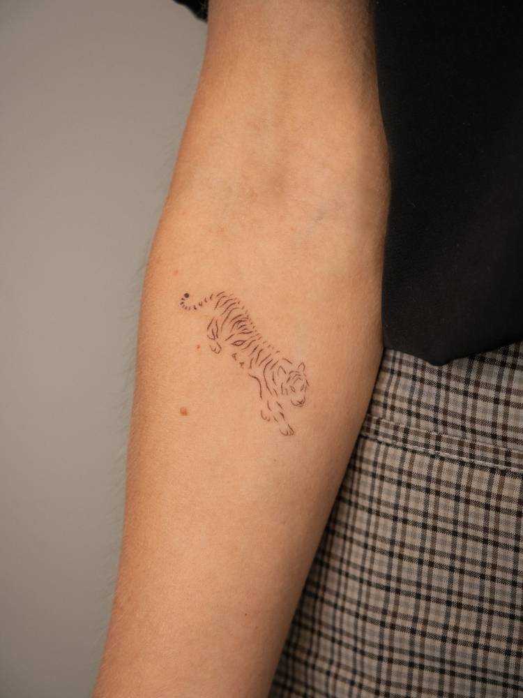 Little tiger tattoo in fine line style located on the inner forearm.