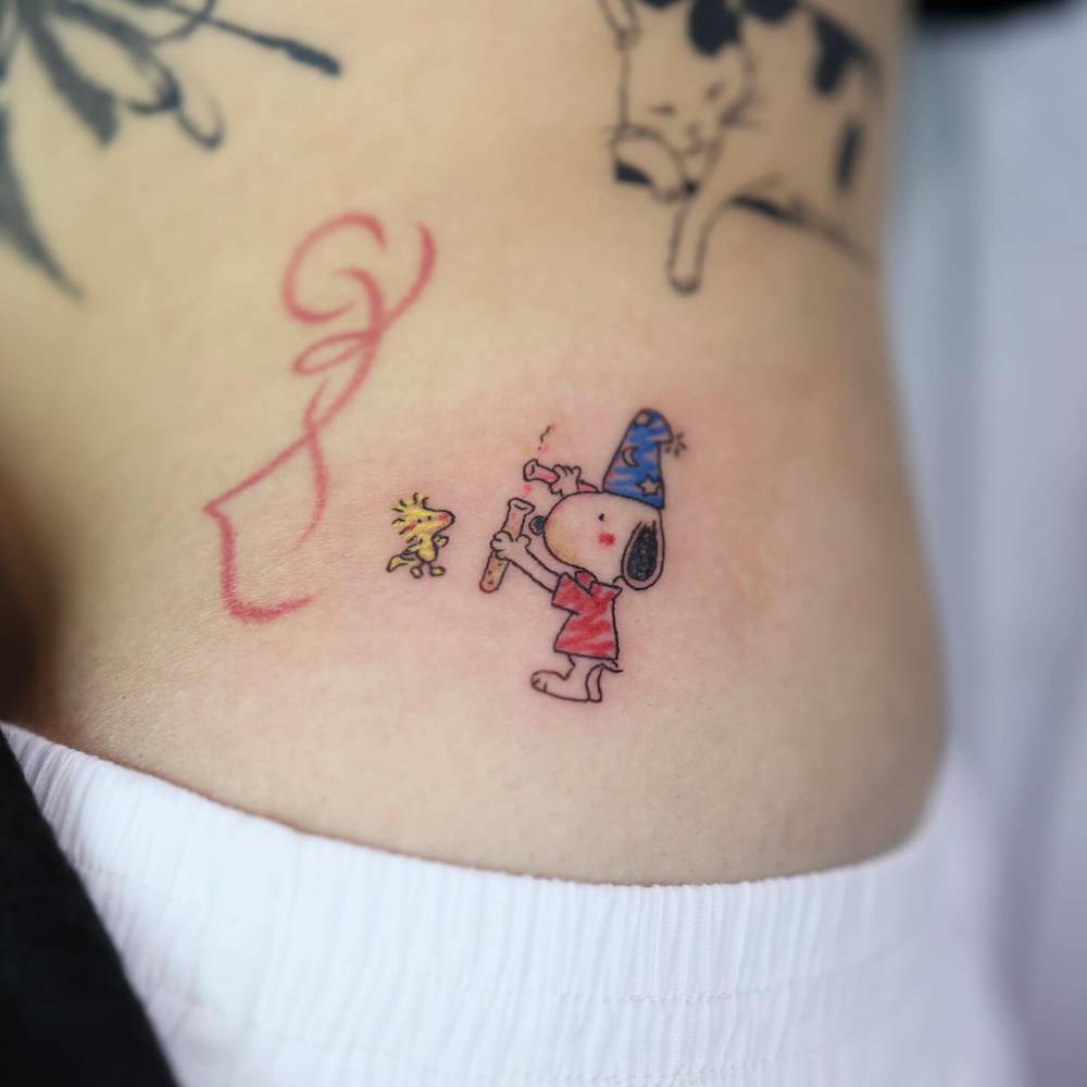 Cartoon style Snoopy and Woodstock tattoo located on the hip.