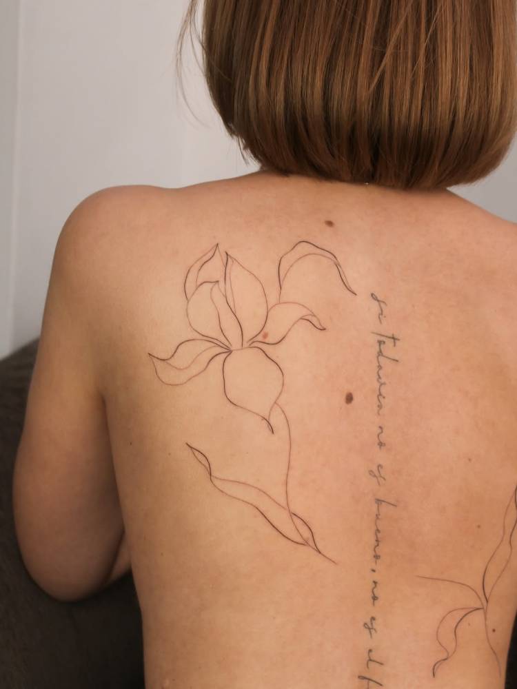 Line art style flower tattoo located on the shoulder blade.