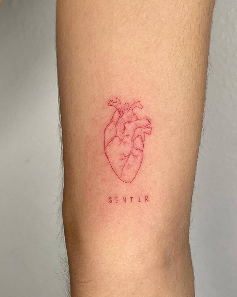 Red anatomical heart and word "sentir" tattooed on the inner arm.