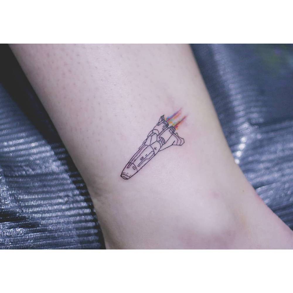 Space shuttle tattoo in fine line style located on the ankle.