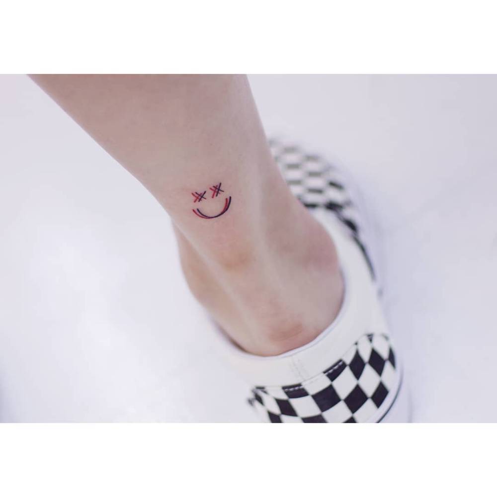 Smiley face tattoo placed on the achilles, minimalistic style.