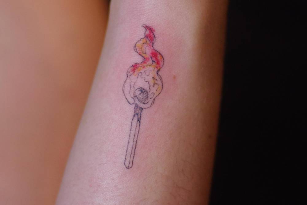 Matchstick tattoo in illustrative style placed on the wrist.