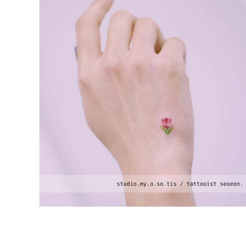 Tiny tulip emoji tattoo located on the hand.