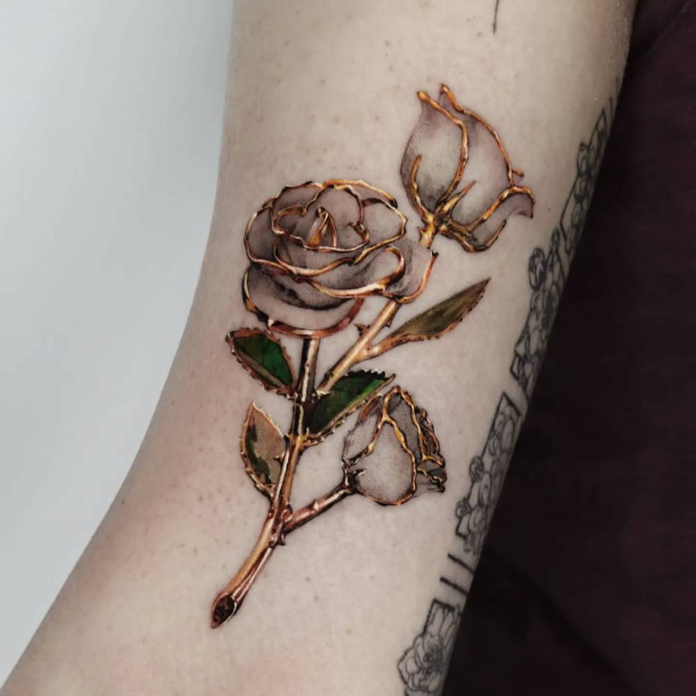 Gold effect white rose tattoo located on the bicep, micro-realistic style.